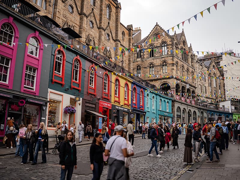 A stone-paved street in Edinburgh with brightly painted buildings bunched up next to each other