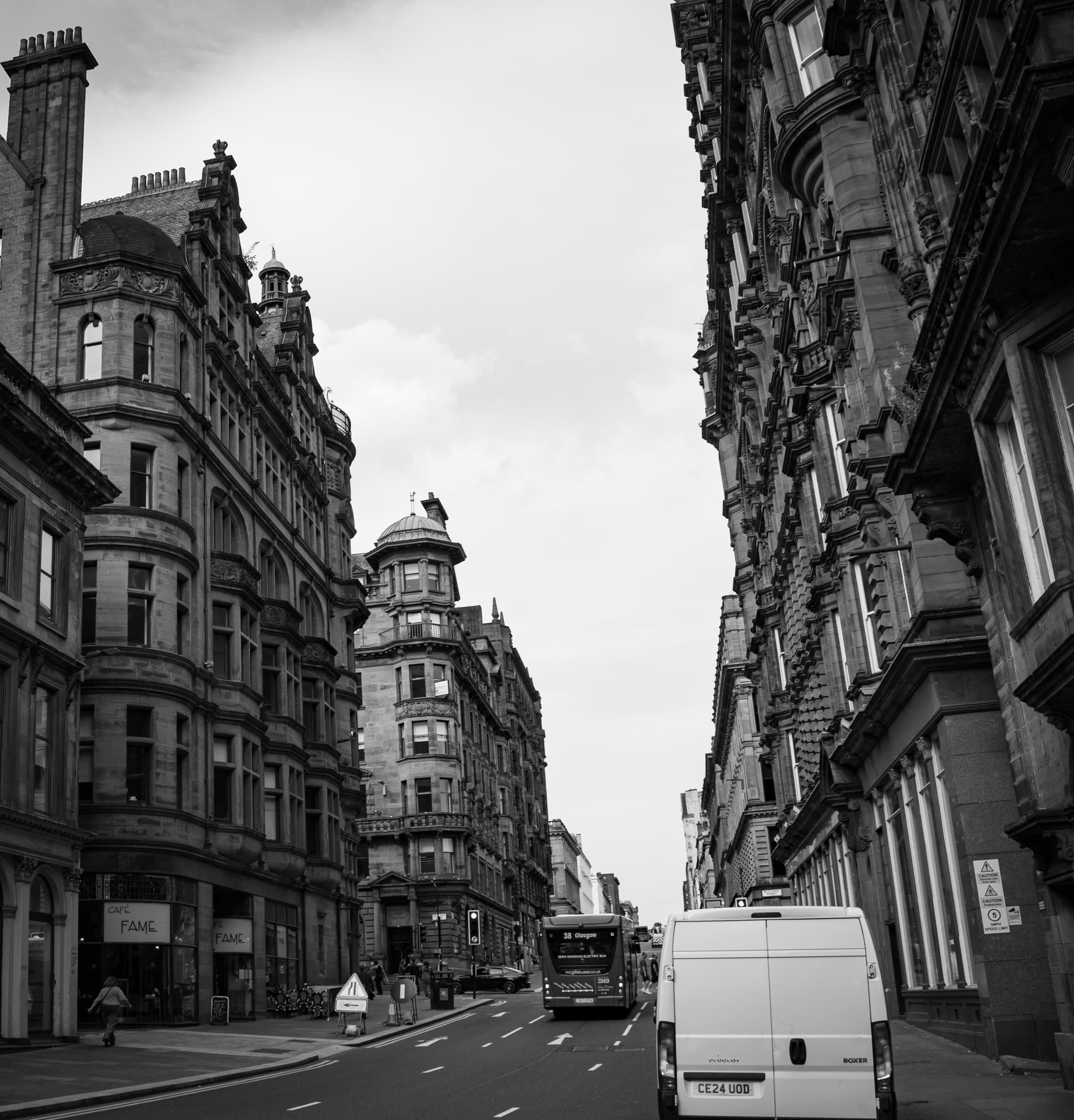 Black and white photo of a street in Glasgow. There are large brick buildings running along each side.