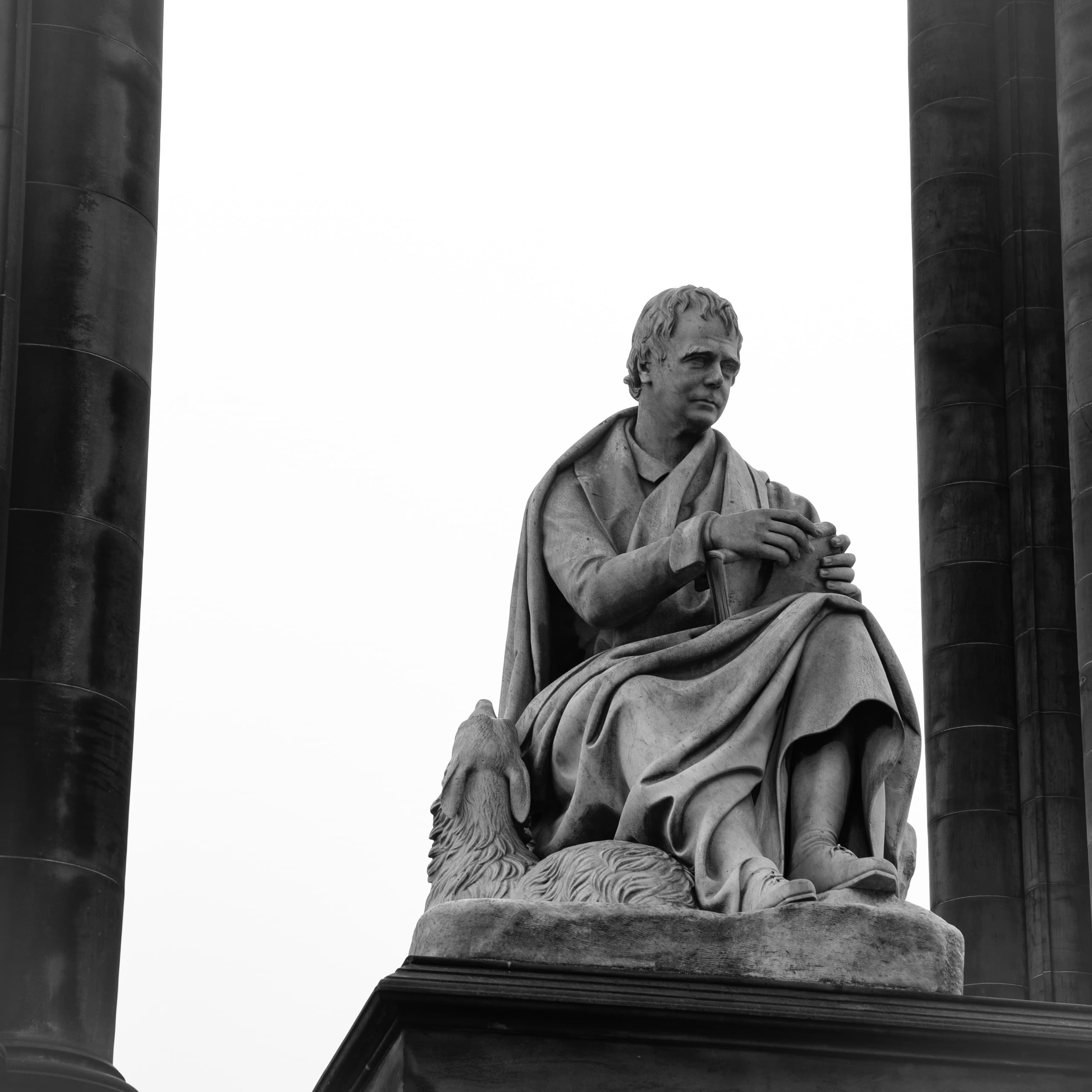 Statue of a man sitting while wearing robes. There are stone columns framing the statue.